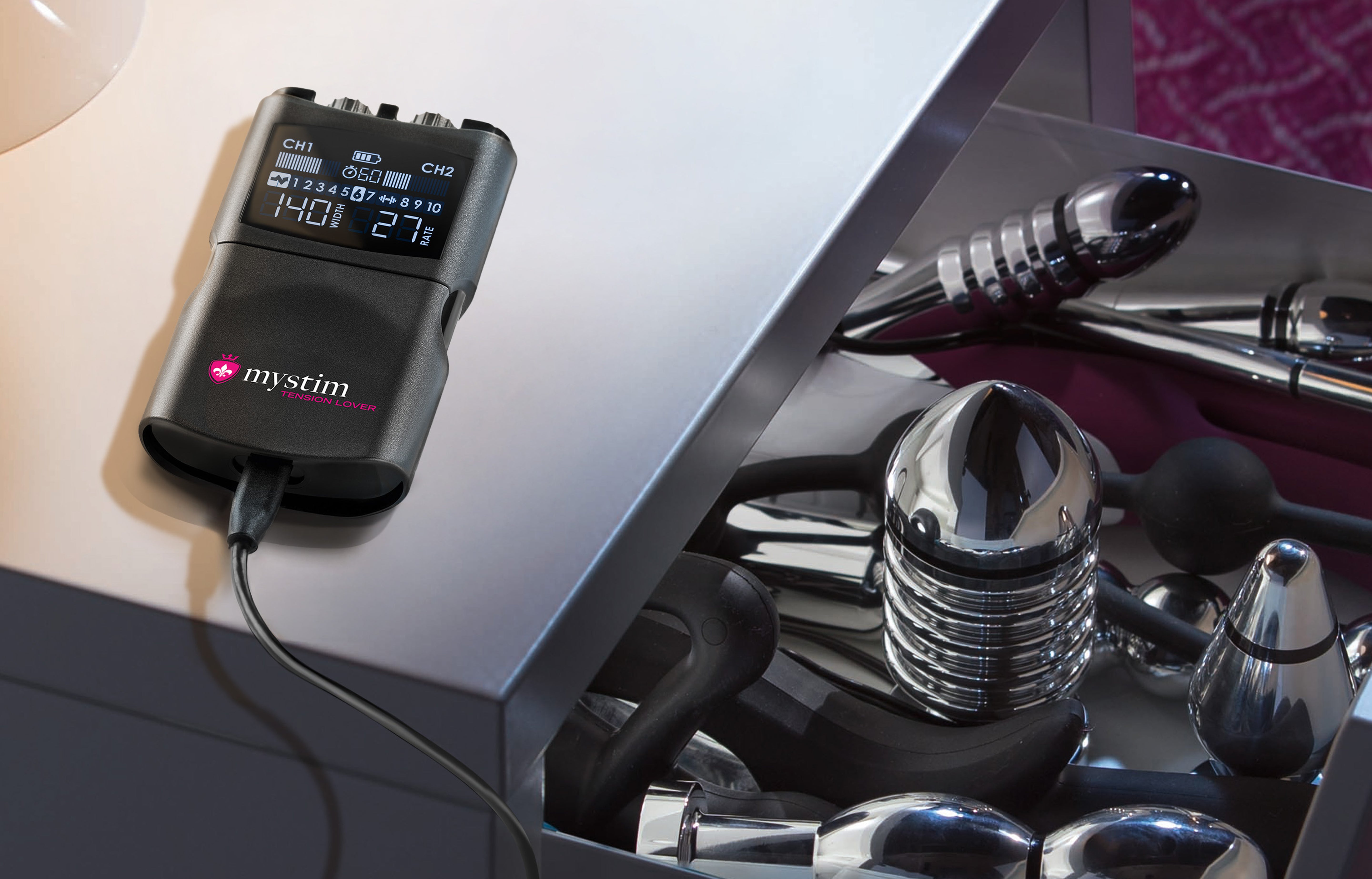 Promo Tension Lover 2 Powerbox zur Elektrostimulation auf Nachttisch mit E-Stim Toys in der Schublade im Closeup